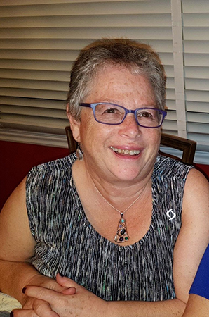 A middle aged, Caucasian women with short grey hair and glasses, smiling at the camera